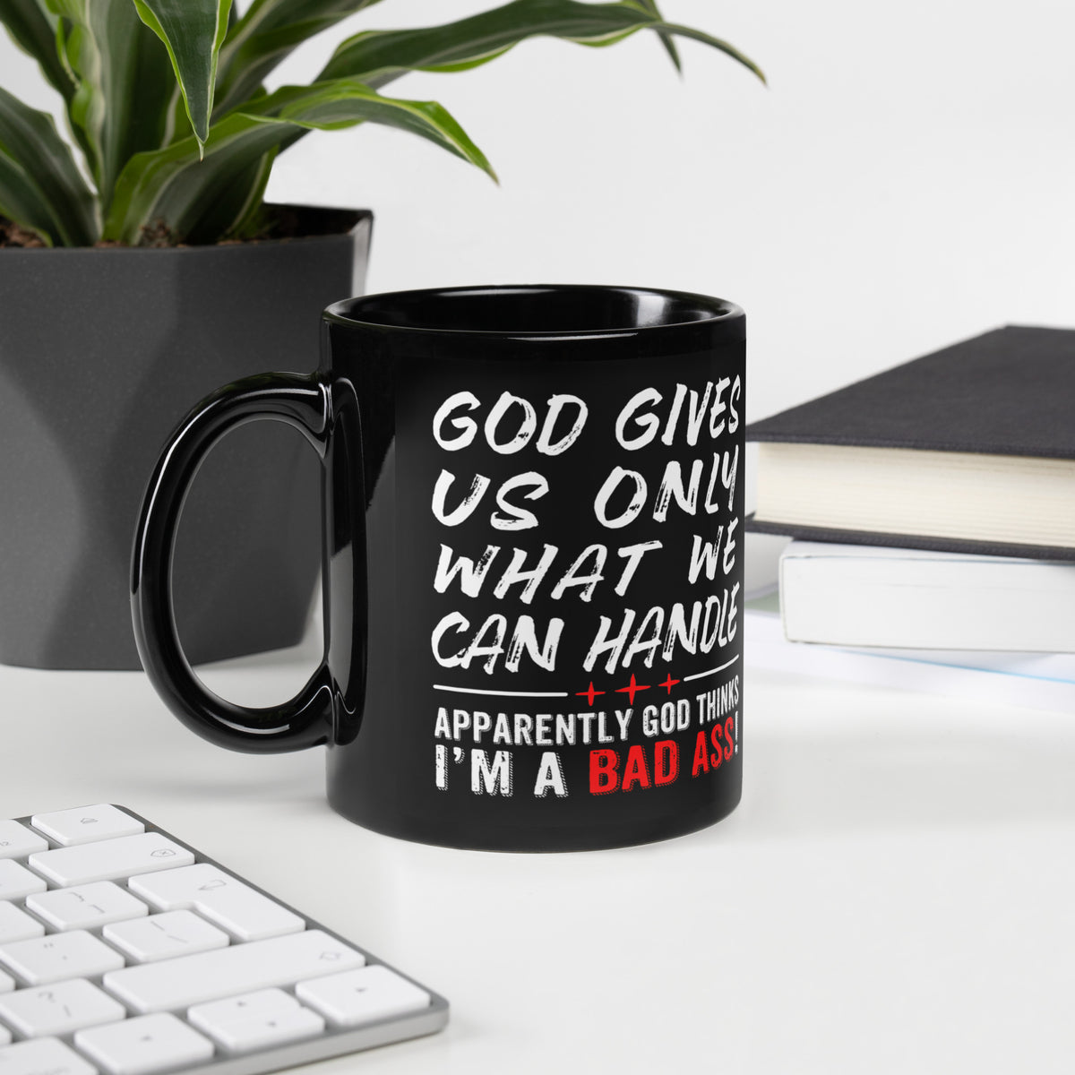 Black God Gives Us Only What We Can Handle 11 oz mug beside a keyboard, plant and notebook, handle on left 