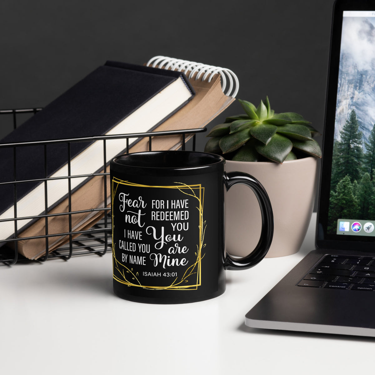 Black Fear Not Isaiah 43:1 mug beside a laptop, notebooks and succulent, handle on right