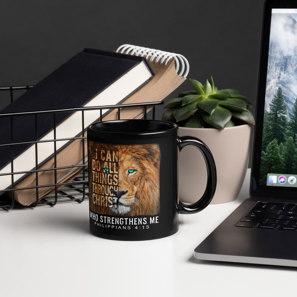 Black Philippians 4:13 lion mug beside a laptop, notebooks and succulent, handle on right