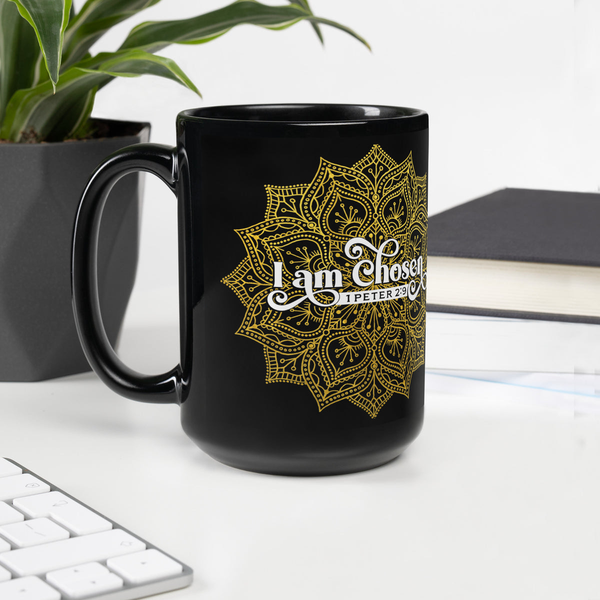 Black I Am Chosen mug beside a keyboard, plant and notebook on a white desk, handle on left