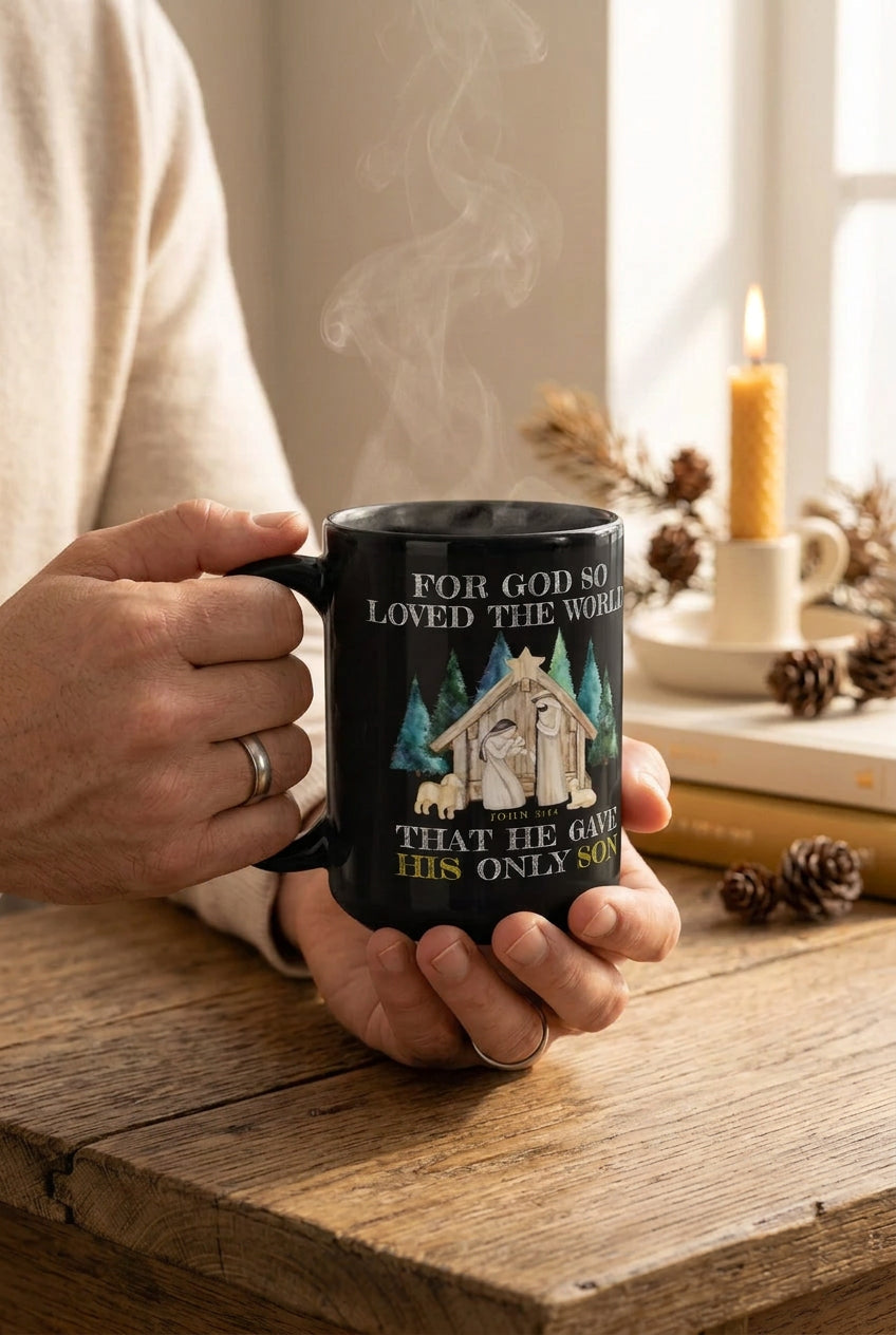 Person holding a black nativity Christmas mug at a wooden table beside a candle and pinecones, handle on the left