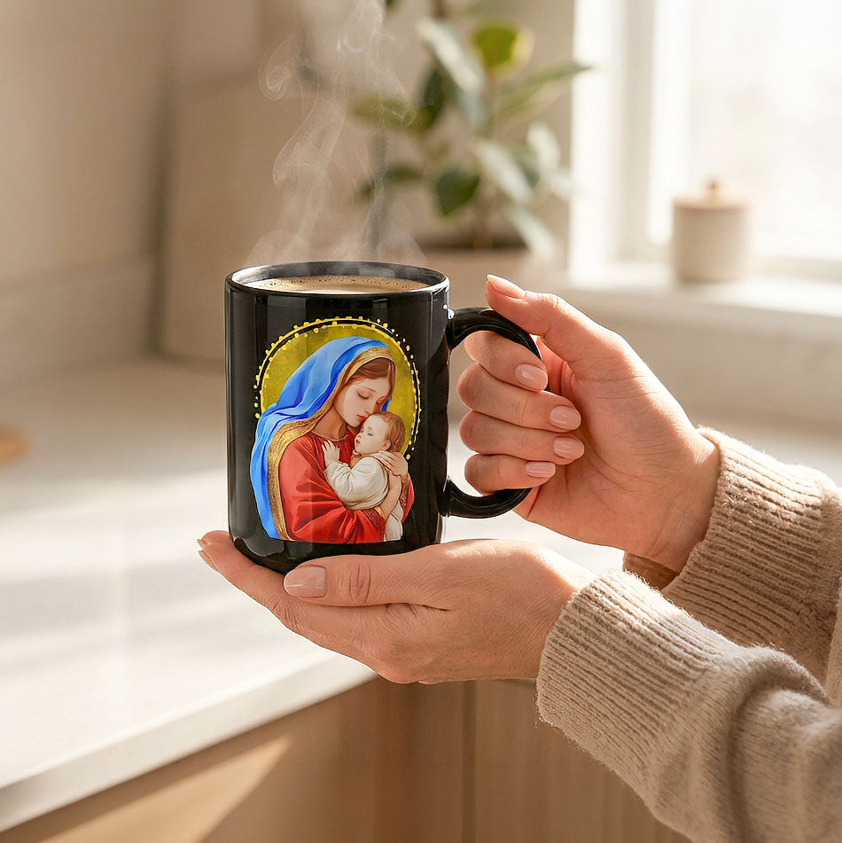 Hands in beige sweater sleeves holding a steaming black Mary and Jesus mug in a sunlit kitchen, handle on the right