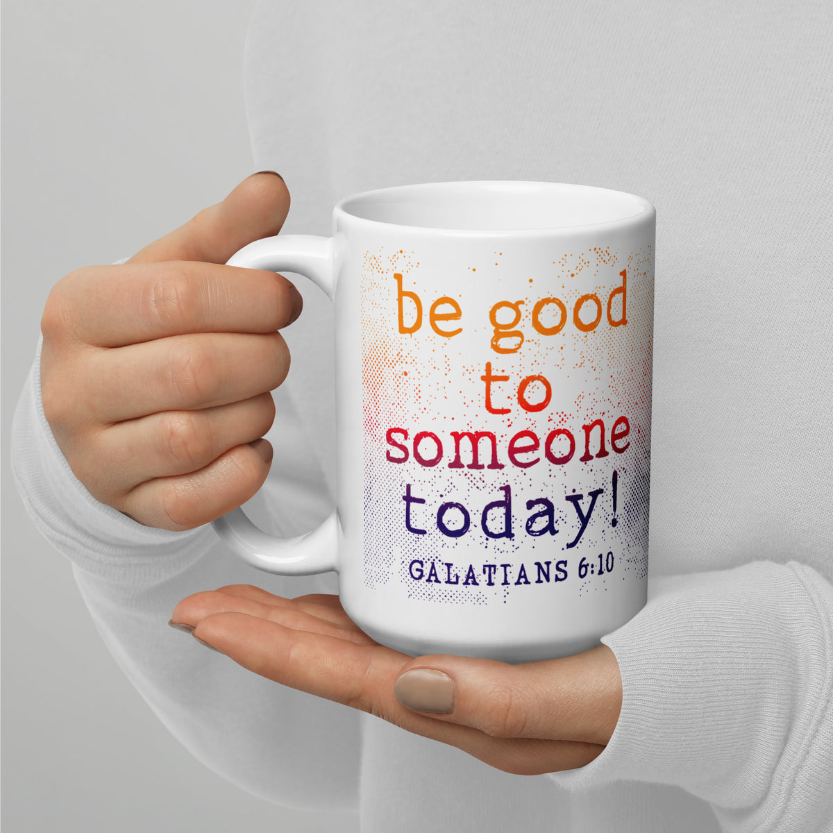 Person holding a white Galatians 6:10 kindness mug with both hands, handle on left