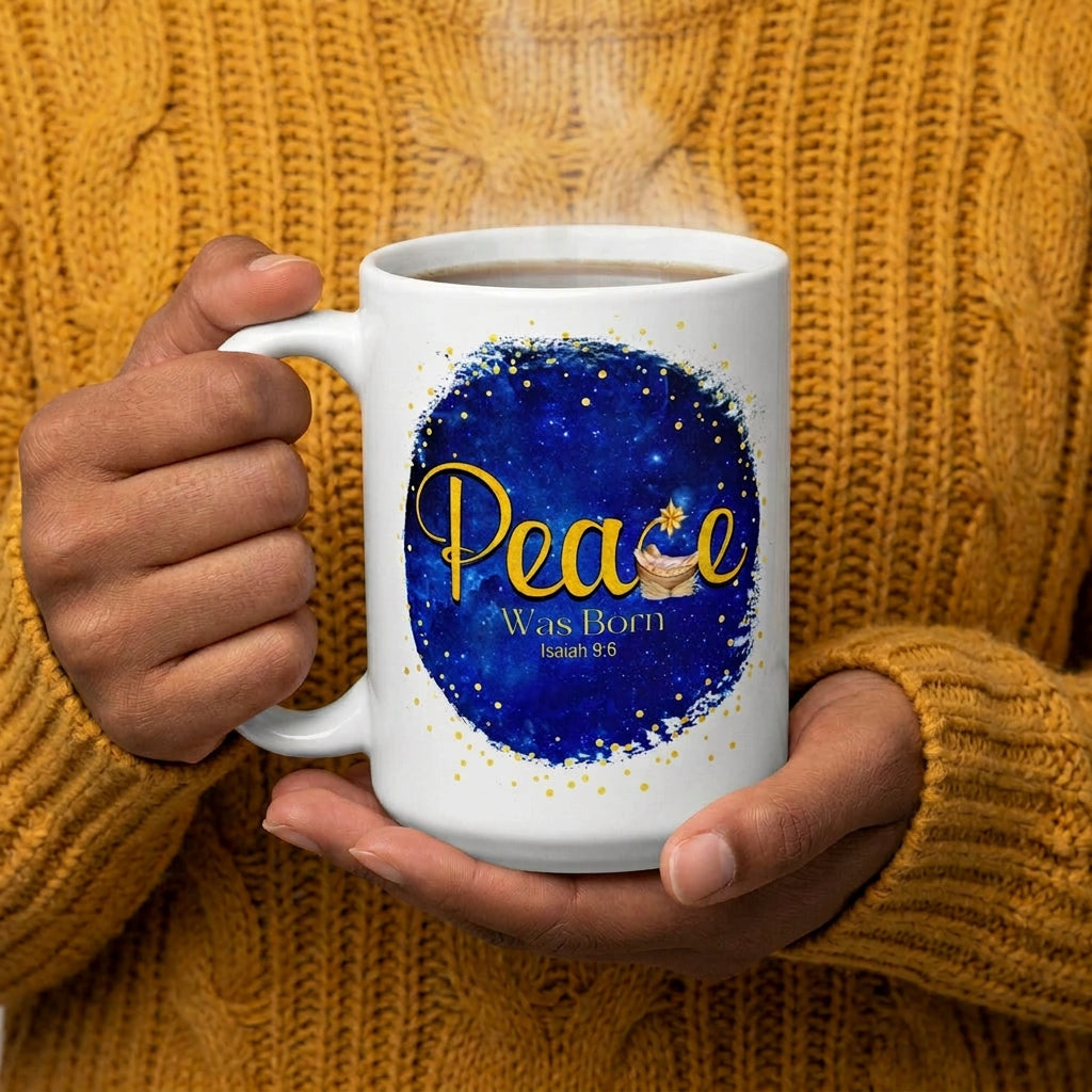 Person in a mustard knit sweater holding a steaming white Peace Was Born Isaiah 9:6 mug, handle on the left
