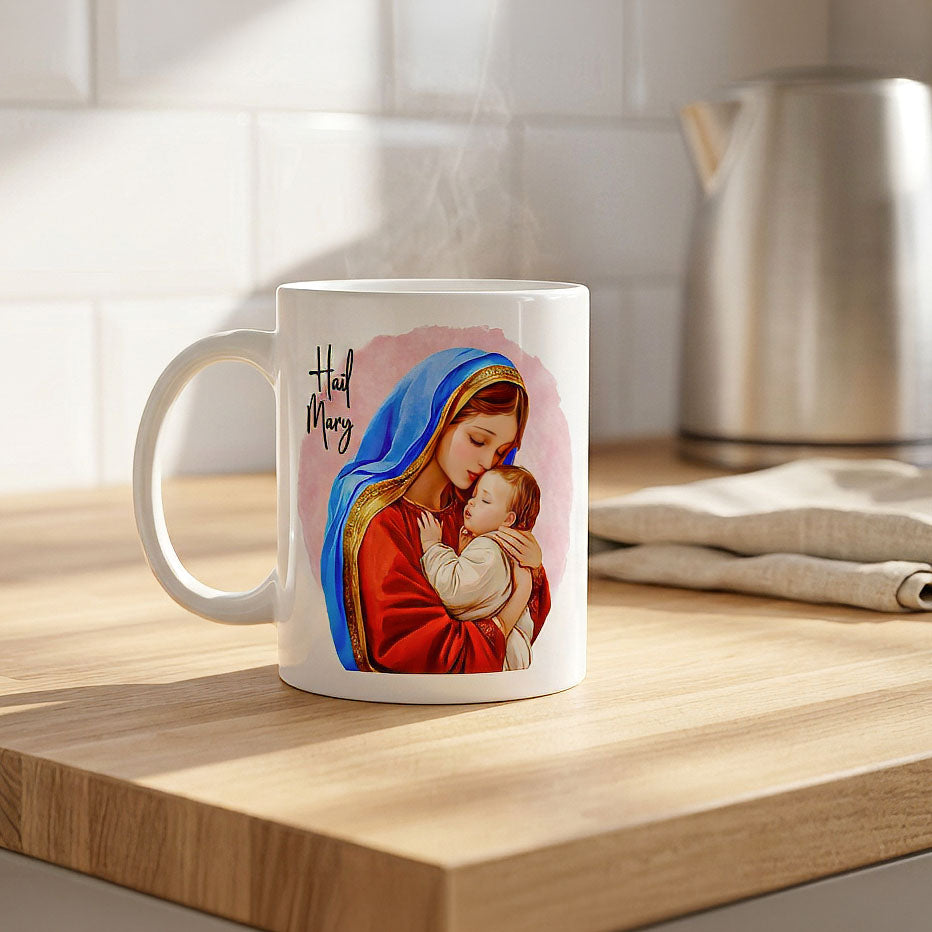Steaming white Hail Mary mug on a wooden kitchen counter beside a kettle and folded cloth, handle on the left