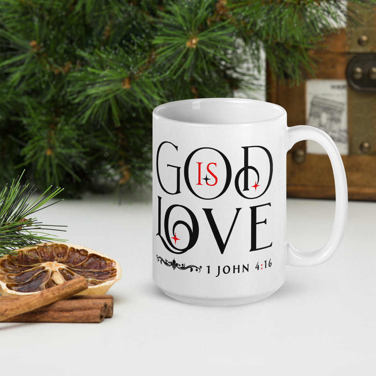 White God Is Love mug beside evergreen branches, dried orange and cinnamon, handle on right