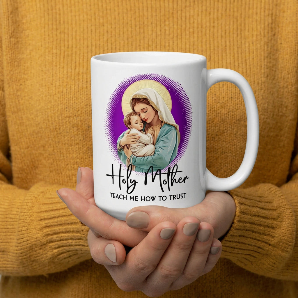 Hands in mustard sweater sleeves cradling a white Holy Mother Teach Me How to Trust mug, handle on the right